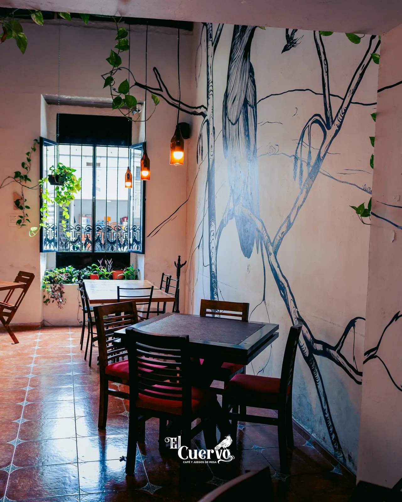 El salón de El Cuervo: el mural de tinta, mesas de madera y la ventana con plantas